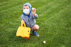 Little boy wearing protective mask hunting for Easter egg in spring garden. photo