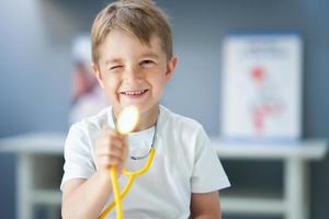 un pequeño doctor con estetoscopio sonriendo en el consultorio del médico foto