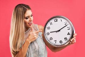 hermosa mujer adulta posando sobre fondo rosa con reloj foto