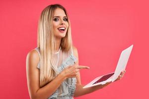 Beautiful adult woman posing over pink background with computer photo