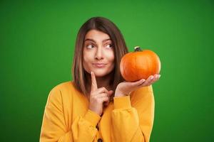 Close up of woman in yellow sweater holding pumpkin over green background photo