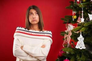 Tired woman decorating Christmas tree over red background photo