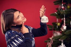 Adult woman decorating Christmas tree over red background photo