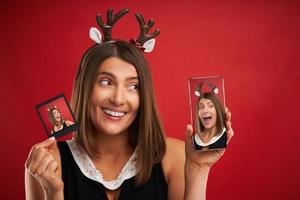 mujer en estado de ánimo navideño comparando imágenes instantáneas con la cámara del teléfono inteligente sobre rojo foto