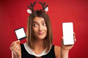 mujer en estado de ánimo navideño comparando imágenes instantáneas con la cámara del teléfono inteligente sobre rojo foto