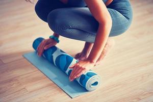 Young woman rolling yoga mat at home photo