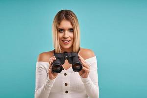 Beautiful adult woman posing over blue background with binoculars photo