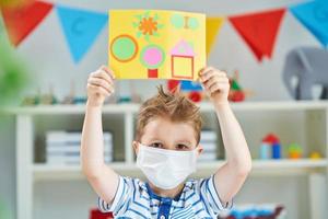 Adorable little boy in kindergarten with mask on due to coronavirus pandemic photo