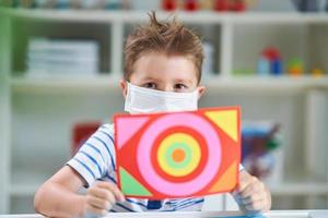 Adorable little boy in kindergarten with mask on due to coronavirus pandemic photo