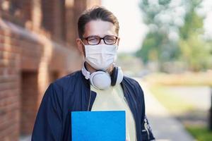 estudiante masculino en el campus con máscara debido a la pandemia del coronavirus foto