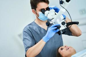 dentista revisando los dientes del paciente con microscopio en la oficina de cirugía foto