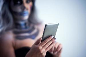 Spooky portrait of woman in halloween gotic makeup holding smartphone photo