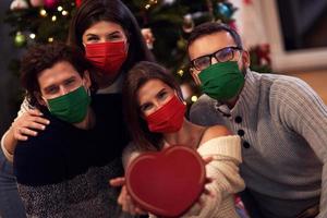 Group of friends wearing masks exchanging Christmas presents at home photo