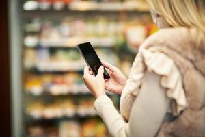 mujer adulta con máscara médica usando un teléfono inteligente y comprando comestibles foto