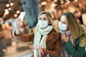 Portrait of two friends shopping together using smartphone and wearing a mask photo