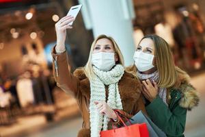 Portrait of two friends shopping together using smartphone and wearing a mask photo