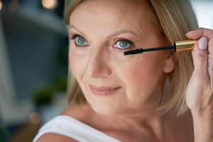 Senior woman applying makeup in the bathroom photo