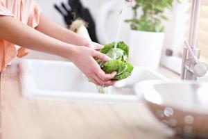 mujer joven lavando lechuga en la cocina moderna foto