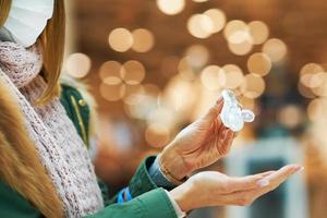 Midsection of adult woman in mall wearing a mask and using hand sanitizer photo