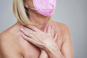 Senior woman in pink mask posing over gray background photo