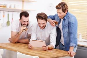 Cheerful friends having fun with smartphone and drinking at home photo