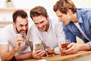 Cheerful friends having fun with smartphone and drinking at home photo