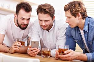 Cheerful friends having fun with smartphone and drinking at home photo