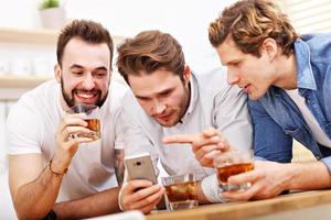 Cheerful friends having fun with smartphone and drinking at home photo