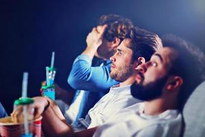 Group of happy friends sitting in cinema watch film and eating popcorn photo