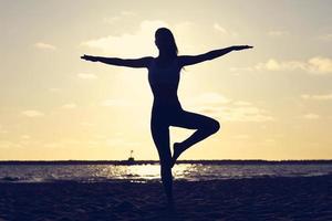 silueta, mujer joven, practicar, yoga, en la playa, en, ocaso foto