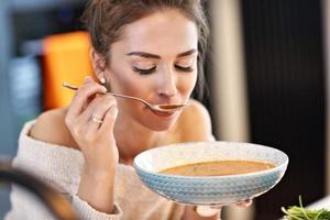 mujer adulta comiendo sopa de calabaza en la cocina foto