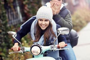 Beautiful young couple smiling while riding scooter in city in autumn photo