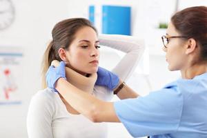 Female doctor putting neck orthopaedic collar on adult injured woman photo