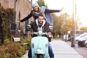 Beautiful young couple smiling while riding scooter in city in autumn photo