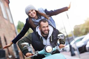 Beautiful young couple smiling while riding scooter in city in autumn photo