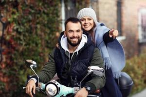 Beautiful young couple smiling while riding scooter in city in autumn photo