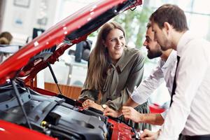 Confident young salesman explaining car features to the young attractive owners photo