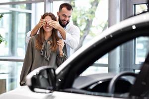Adult man making surprise to beautiful woman in car showroom photo