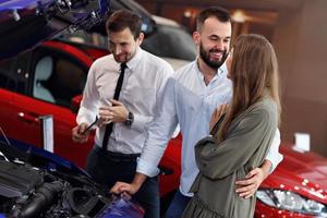 Confident young salesman explaining car features to the young attractive owners photo