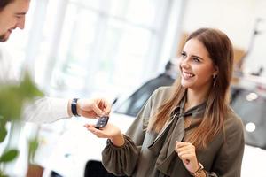 Happy young woman buying car in showroom photo