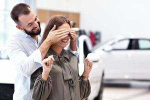 Adult man making surprise to beautiful woman in car showroom photo