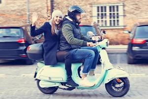 Beautiful young couple smiling while riding scooter in city in autumn photo