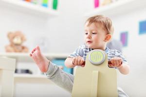 Cheerful baby boy swinging on a rocking chair in the shape of a scooter photo