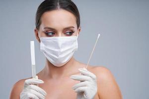 Portrait of beautiful woman holding swab in mask on gray background photo