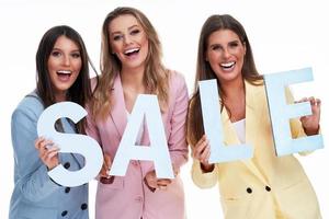 Three women in pastel suits holding sale letters over white background photo