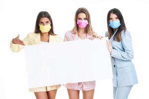 Three women in pastel suits holding billboard posing over white background photo