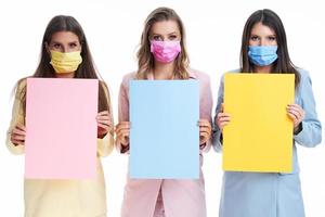 Three women in pastel suits holding billboard posing over white background photo