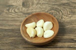 Peeled garlic on wooden bowl and wood table background. Natural photo concept.