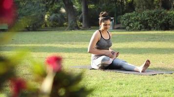 Video footage of a woman sitting in lotus pose and taking deep breaths in the fresh air in a park.