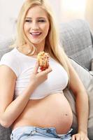 bella joven embarazada comiendo pastel en casa foto